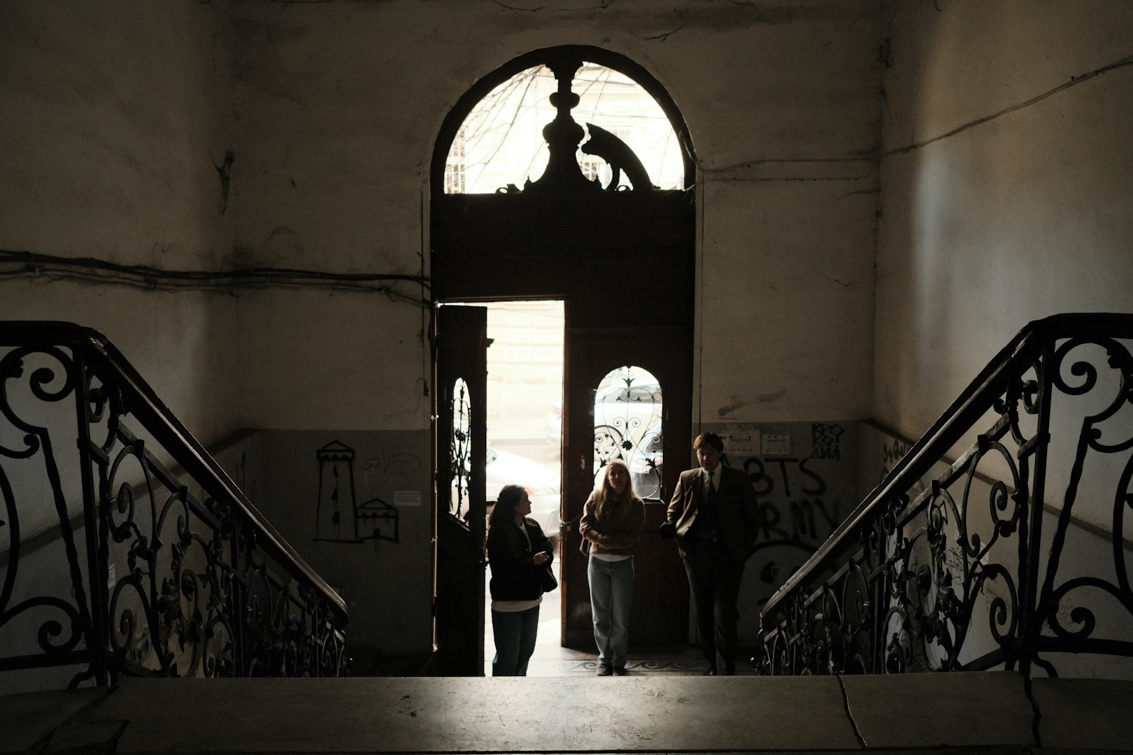 Silhouetted figures stand near an open doorway with stairs